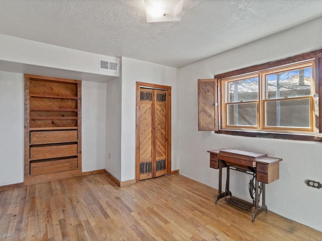 unfurnished bedroom featuring a textured ceiling, baseboards, visible vents, and light wood-style floors