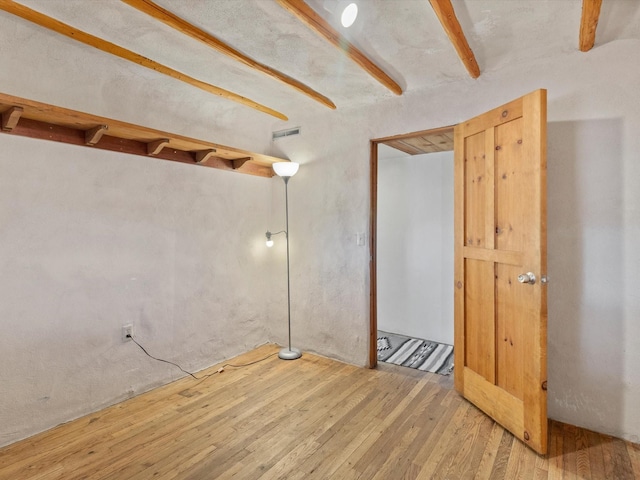 empty room featuring beamed ceiling, wood-type flooring, and visible vents