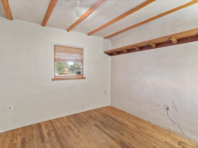 spare room featuring beamed ceiling and wood-type flooring