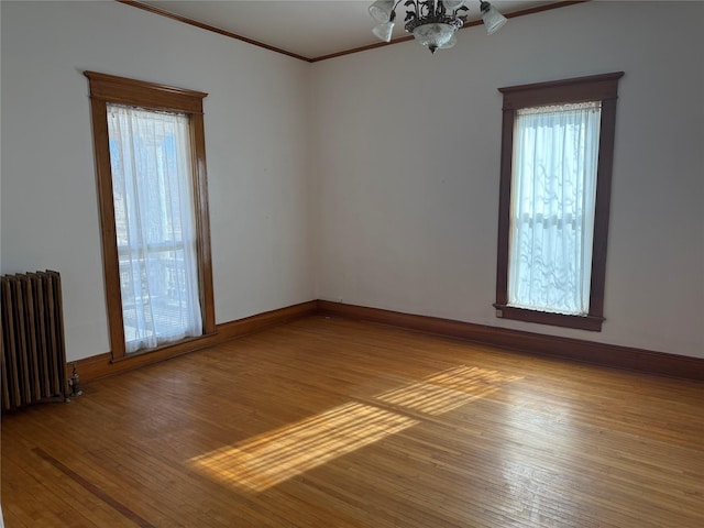 empty room with light wood-type flooring, an inviting chandelier, crown molding, and radiator heating unit