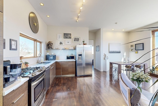 kitchen featuring stainless steel appliances, backsplash, track lighting, dark hardwood / wood-style flooring, and sink