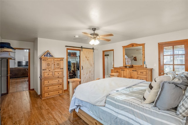 bedroom with a spacious closet, light hardwood / wood-style floors, a closet, ceiling fan, and a barn door