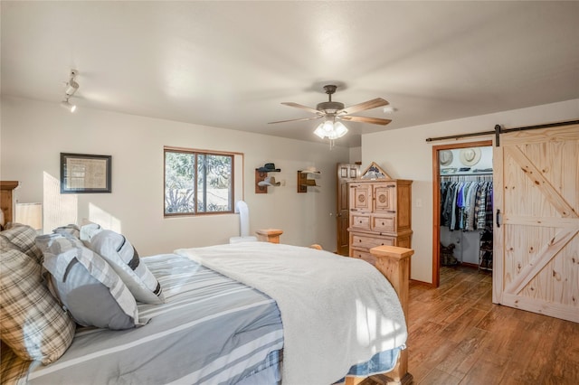 bedroom with ceiling fan, a barn door, hardwood / wood-style flooring, a spacious closet, and a closet