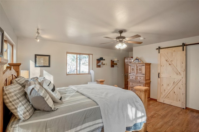 bedroom with ceiling fan, a barn door, light hardwood / wood-style floors, and rail lighting