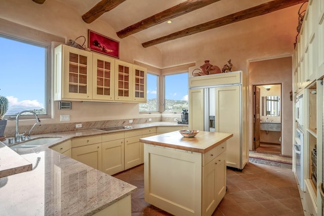 kitchen featuring sink, paneled built in fridge, black electric stovetop, light stone countertops, and a center island