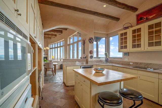 kitchen featuring a center island, beamed ceiling, sink, cream cabinetry, and a breakfast bar