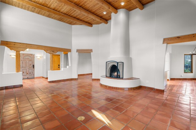 unfurnished living room featuring wood ceiling, tile patterned flooring, beam ceiling, a towering ceiling, and a fireplace