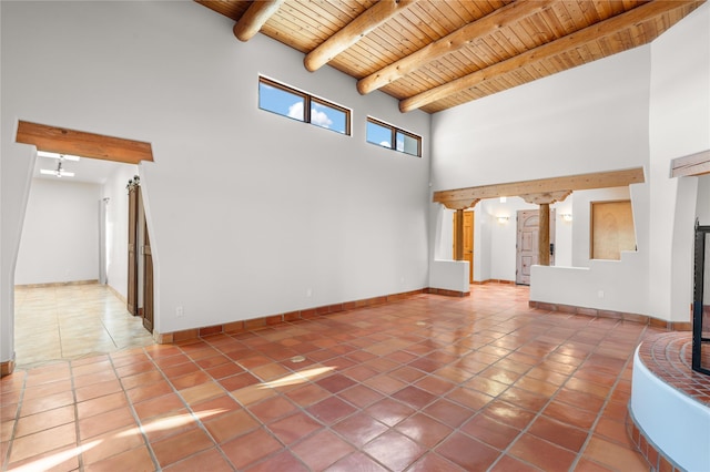 unfurnished living room with a towering ceiling, an inviting chandelier, wood ceiling, tile patterned floors, and beam ceiling