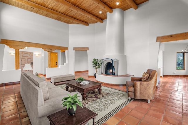 tiled living room featuring wood ceiling, a high ceiling, beam ceiling, and a large fireplace