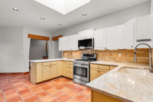 kitchen with kitchen peninsula, appliances with stainless steel finishes, sink, backsplash, and a skylight