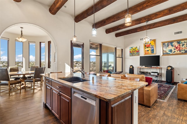 kitchen featuring light stone countertops, a kitchen island with sink, stainless steel dishwasher, sink, and decorative light fixtures