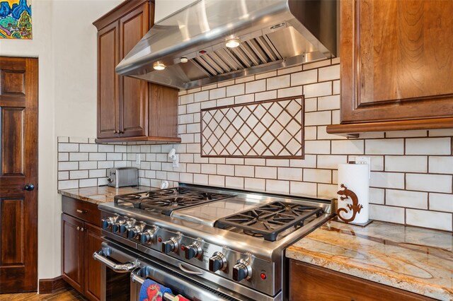 kitchen with double oven range, light stone counters, wall chimney exhaust hood, and decorative backsplash