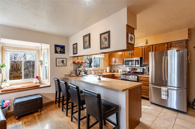 kitchen featuring kitchen peninsula, appliances with stainless steel finishes, backsplash, a textured ceiling, and a breakfast bar area