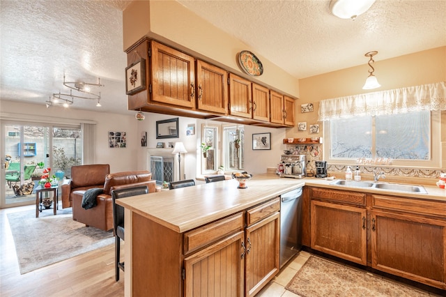 kitchen featuring a textured ceiling, decorative light fixtures, sink, kitchen peninsula, and stainless steel dishwasher