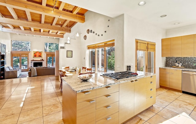 kitchen with stainless steel appliances, a center island, light stone counters, tasteful backsplash, and light brown cabinets