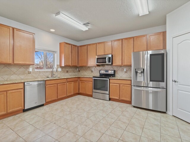 3110 Floras Del Sol, Santa Fe, NM 87507 - kitchen featuring a textured ceiling, appliances with stainless steel finishes, decorative backsplash, sink, and light stone counters