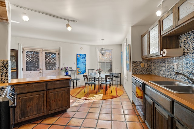 kitchen featuring decorative light fixtures, sink, backsplash, light tile patterned floors, and stainless steel range oven