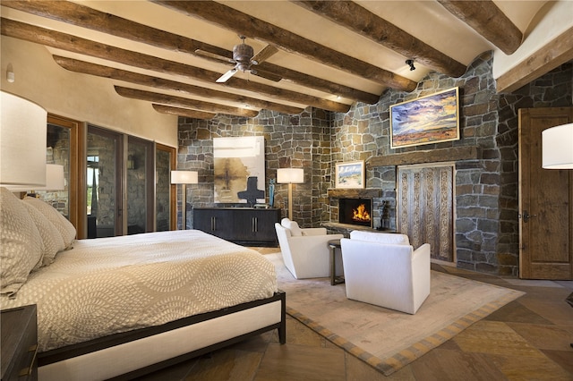 bedroom with beamed ceiling, a stone fireplace, and ceiling fan