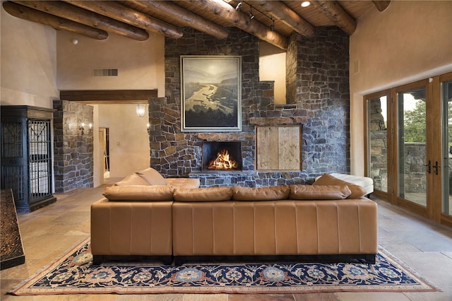 living room with beam ceiling, a stone fireplace, a high ceiling, and wood ceiling