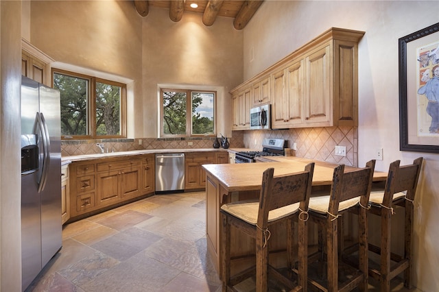 kitchen featuring appliances with stainless steel finishes, a towering ceiling, beamed ceiling, butcher block counters, and decorative backsplash