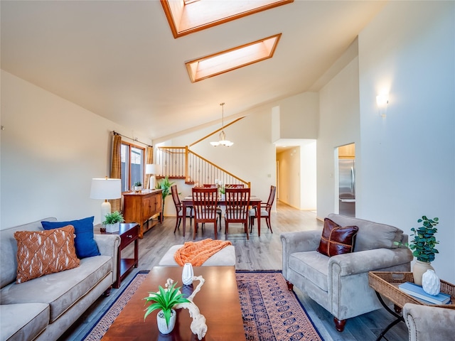 living room featuring hardwood / wood-style floors, a notable chandelier, high vaulted ceiling, and a skylight