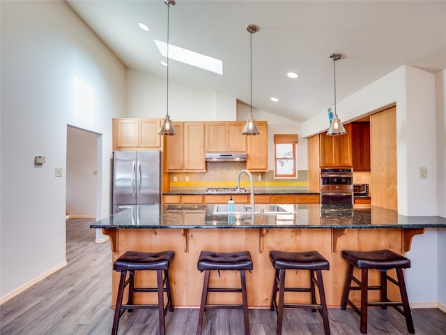 kitchen featuring a breakfast bar area, appliances with stainless steel finishes, a skylight, tasteful backsplash, and decorative light fixtures