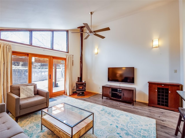 living room with ceiling fan, high vaulted ceiling, light wood-type flooring, and a wood stove