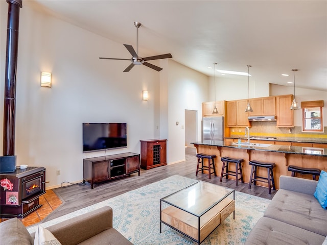 living room featuring lofted ceiling, a wood stove, sink, ceiling fan, and light wood-type flooring