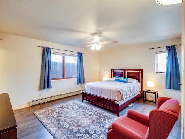 bedroom with multiple windows, a baseboard heating unit, hardwood / wood-style floors, and ceiling fan