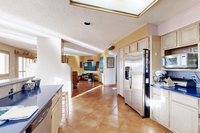 kitchen with appliances with stainless steel finishes, cream cabinets, a textured ceiling, and light tile patterned floors