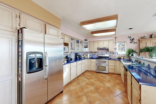 kitchen with sink, appliances with stainless steel finishes, a textured ceiling, light tile patterned flooring, and decorative backsplash