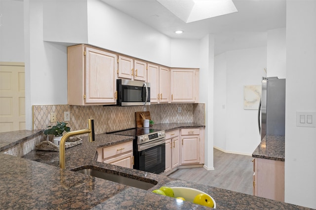 kitchen with backsplash, light brown cabinets, dark stone counters, and appliances with stainless steel finishes