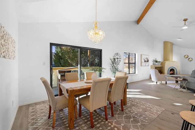 dining area featuring wood-type flooring, high vaulted ceiling, a large fireplace, beam ceiling, and ceiling fan with notable chandelier