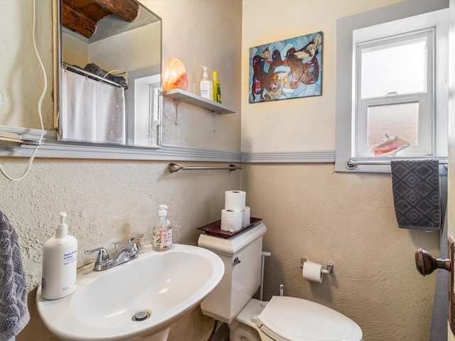 bathroom with a textured wall, a sink, toilet, and curtained shower