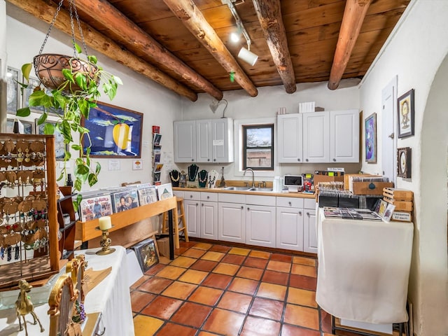 kitchen featuring beamed ceiling, white cabinetry, sink, and wood ceiling