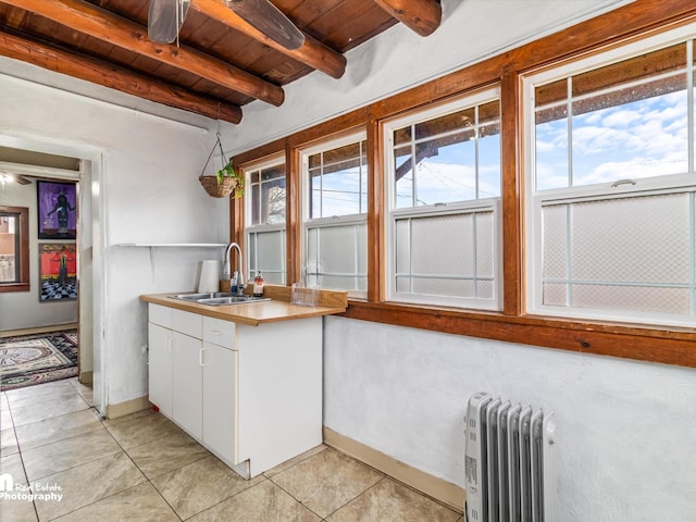 kitchen with wooden ceiling, radiator, a healthy amount of sunlight, beam ceiling, and white cabinets