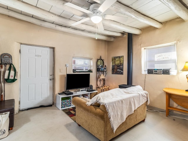 living room featuring beamed ceiling, a wood stove, and ceiling fan