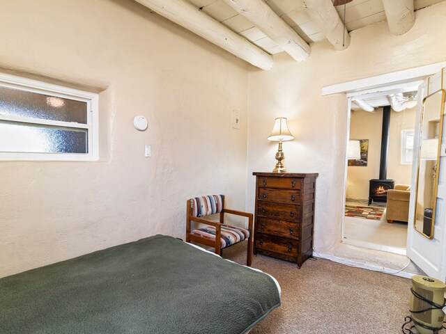 carpeted bedroom with beam ceiling and a wood stove