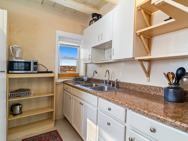 kitchen featuring open shelves, stainless steel microwave, a sink, dark countertops, and white cabinets