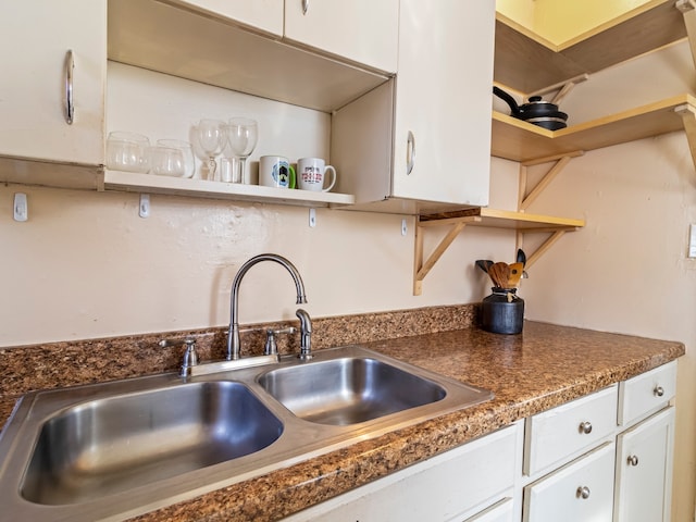 kitchen featuring white cabinetry, dark countertops, a sink, and open shelves