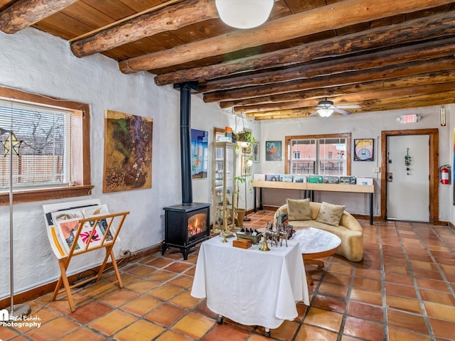 living room featuring wooden ceiling, a wood stove, beamed ceiling, ceiling fan, and tile patterned flooring