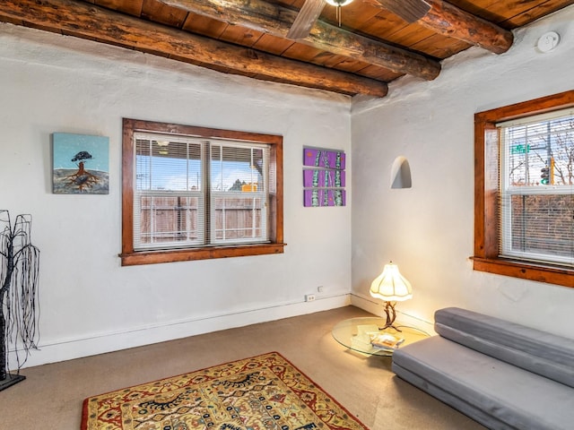 living area with baseboards, beamed ceiling, carpet, and wooden ceiling