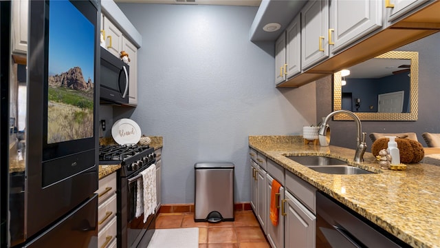 kitchen featuring sink, white cabinetry, light stone counters, light tile patterned floors, and black appliances