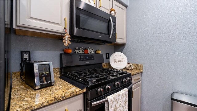 kitchen featuring gas stove, stone countertops, and white cabinets