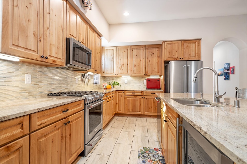 kitchen with sink, light stone counters, tasteful backsplash, stainless steel appliances, and beverage cooler