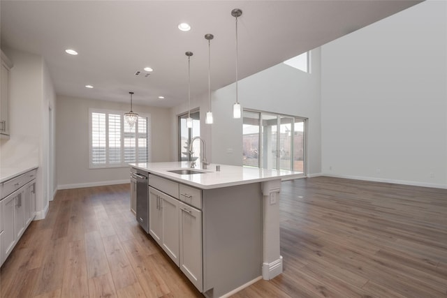 kitchen with pendant lighting, sink, a center island with sink, stainless steel dishwasher, and light wood-type flooring