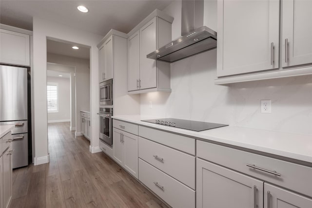 kitchen featuring stainless steel appliances, light hardwood / wood-style flooring, white cabinets, and wall chimney exhaust hood