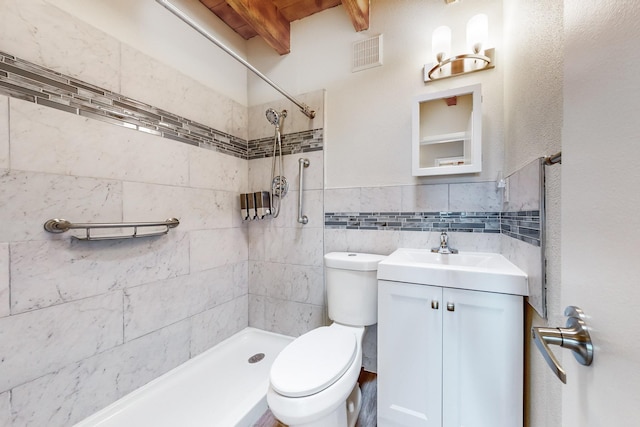 bathroom with a tile shower, beamed ceiling, tile walls, vanity, and toilet