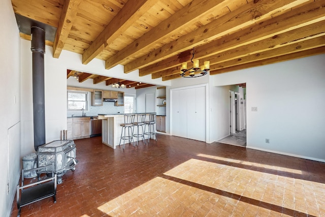 unfurnished living room featuring sink, a notable chandelier, beamed ceiling, and a wood stove