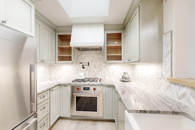 kitchen with light stone counters, tasteful backsplash, stainless steel appliances, and custom range hood